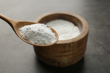 Spoon of baking powder over bowl at grey textured table, closeup. Space for text