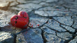 A red stone heart smashed in a cracked concrete ground as a symbol for a broken heart and lovesickness 