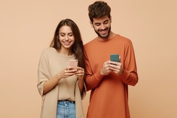 Young smiling happy couple two friends family man woman wear casual clothes hold in hand use mobile cell phone together chatting isolated on pastel plain light beige color background studio portrait 