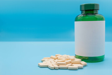 Medicine bottle with blank label, next to a stack of pills isolated on blue background with copy space