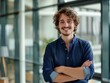 © yj - A smiling confident young business man standing with arms crossed in a modern office. a happy handsome curly haired male entrepreneur with his hands folded across his chest. generative AI
