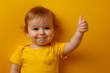 © Sariyono - Smiling toddler giving a thumbs up in a bright yellow shirt, capturing the wholesome innocence and approval of early childhood