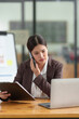 © crizzystudio - Asian businesswoman Company sales manager while talking on the phone with a customer, looking at documents, files, financial details, agreements, and business contracts on a laptop in the office.