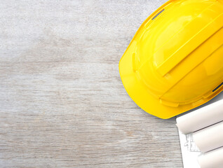 Yellow safety helmet or hard hat and construction paper plans on wood table background.