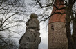 Eine aus Stein gemeißelte Skulptur eines Mannes, der ein Kind auf den Schultern trägt, blickt in Richtung eines alten, mittelalterlichen Turms