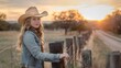 © yj - a beautiful high school senior stand posing next to a ranch fence, country look, she is wearing a cowboy hat and boots, country girl,    sunset. generative AI