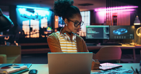 Fototapete - Black Female Specialist is Writing Business Strategy, Using Digital Tablet to Take Notes in Creative Office Environment. Young Project Manager with Headphones Working on Laptop Computer 