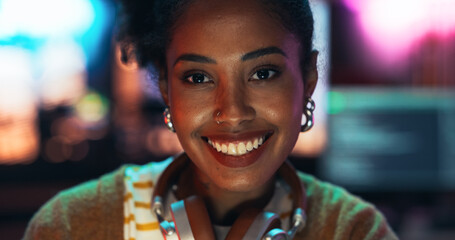 Poster - Portrait of a Stylish Young Black Woman with Headphones, Looking at Camera, and Smiling in a Creative Office. Beautiful Diverse Female Working for her Dream Agency, Feeling Empowered