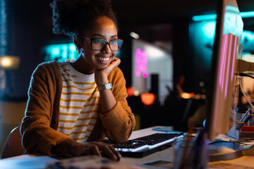 Aufkleber - African American Female Smiling While Checking Data and Statistic Charts Using Desktop Computer.  Portrait of a Happy Successful Black Businesswoman in Creative Agency in the Evening