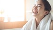 A Closeup head shot of a young beautiful Asian woman applying facial moisturizer after bathing. Smiling beautiful woman wrapped in towel to smooth her skin Daily routine in the morning.