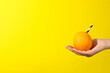 Orange with cocktail straw on hand on yellow background, space for text