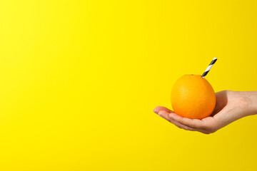 Sticker - Orange with cocktail straw on hand on yellow background, space for text