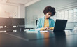 © Flamingo Images - Young black businesswoman using a laptop while working after hours at her desk in a office
