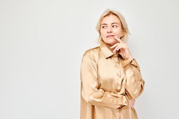 Thoughtful woman in beige shirt posing with hand on chin against a light grey background.