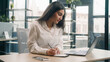 © Yuliia - Business woman Arabian Indian girl businesswoman manager laptop computer work writing notebook notes ideas write working showing thumb up recommend online service support at camera smiling in office