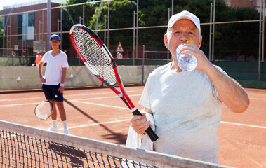 Mature man drink water on tennis court