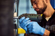 © bnenin - A mechanic using a drill to screw the wheels on a car, wearing protective gloves.