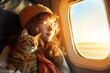 A young girl owner holds a cat in the airplane cabin near the window during the flight. Vacation, travel and moving concept with pet. Traveling with a cat by plane. Traveling cat