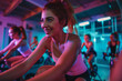Positive sporty girl riding indoor stationary bike during cycling class with her female friends in cycling studio.