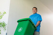 © Mdv Edwards - A middle aged asian janitor bringing out the plastic mobile trash bin outside the building.