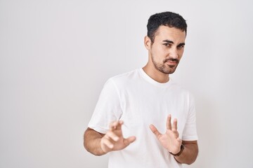 Wall Mural - Handsome hispanic man standing over white background disgusted expression, displeased and fearful doing disgust face because aversion reaction.