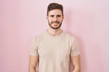 Poster - Hispanic man with beard standing over pink background with hands together and crossed fingers smiling relaxed and cheerful. success and optimistic