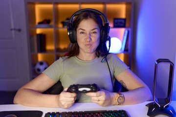 Sticker - Beautiful brunette woman playing video games wearing headphones puffing cheeks with funny face. mouth inflated with air, crazy expression.