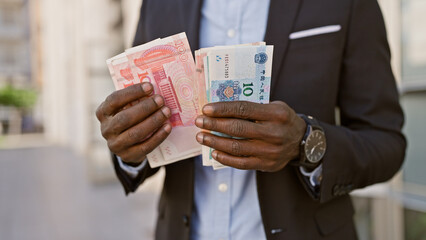 Wall Mural - African man in suit holding chinese yuan and other currency on city street