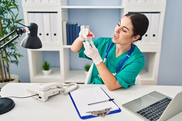 Canvas Print - Young beautiful hispanic woman doctor holding test tube speaking at clinic