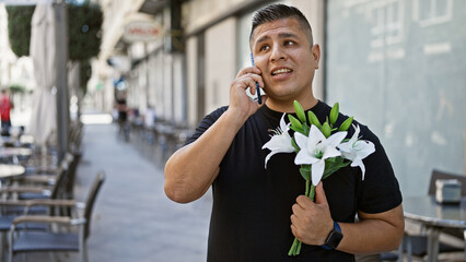 Wall Mural - Young latin man's portrait outdoors, a cool, casually dressed guy talking on his phone on an urban city street, holding a beautiful bouquet of spring flowers, expression serious yet relaxed.