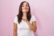 Middle age brunette woman standing over pink background thinking concentrated about doubt with finger on chin and looking up wondering