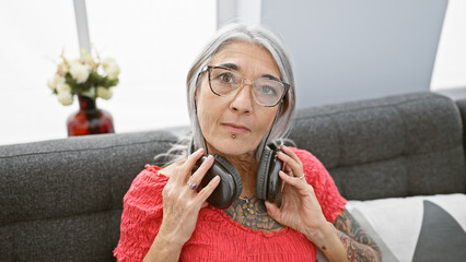 Poster - Serene middle age woman, grey-haired and beautiful, immerses in music, relaxing on a cozy sofa at home, wearing headphones, epitome of comfort, resting while donning a serious expression.