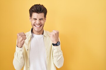 Canvas Print - Young hispanic man standing over yellow background excited for success with arms raised and eyes closed celebrating victory smiling. winner concept.