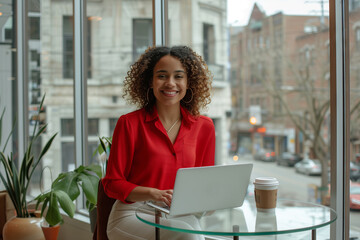 A woman is sitting at a table with a laptop, smiling next to a houseplant in a flowerpot. There is a tree outside the building. A travel theme with tableware decor