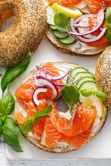 Wall Mural - Salmon sandwiches with bagel, salted fish, fresh cucmber, onion and basil on white background, top view. Healthy breakfast with salmon toasts