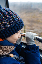 Close-up of a boy wearing gloves looking out of the window and holding railings in a cable car, Georgia