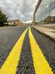 Freshly painted two yellow line or double yellow lines on a newly made road, warning vehicle users that parking is not permitted at anytime.  No parking warning anytime on this section of UK road.