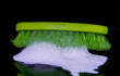Green hard brush in soap foam against a black background