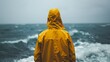 Person in yellow raincoat gazes at the vast ocean