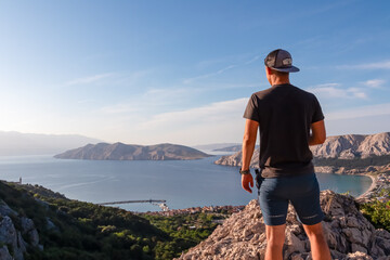 Wall Mural - Hiker man on edge of rock cliff overlooking archipelago of Kvarner Bay in coastal town Baska, Krk Island, Primorje-Gorski Kotar, Croatia, Europe. Coastal hiking trail along coastline of Adriatic Sea