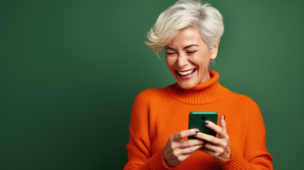 Canvas Print - An elderly woman smiling and laughing with her phone against green background.