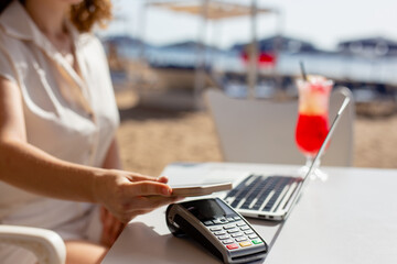 Young woman paying with mobile phone sitting on beach