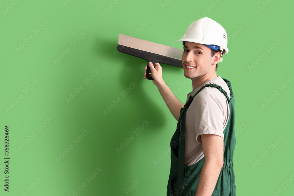Male worker with putty knife on green background