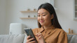 © Yuliia - Asian chinese korean businesswoman woman girl freelancer work from home in kitchen read good news smiling use mobile phone choose goods on internet order delivery online typing message cellphone chat
