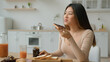 © Yuliia - Asian korean woman eat sweet sandwich at home chinese girl female housewife cooking breakfast with bread and chocolate paste order food from supermarket delivery enjoy taste eating dessert in kitchen