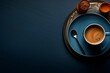A cup of coffee with cream stand on a plate with a silver spoon next to it, on a dark blue surface.