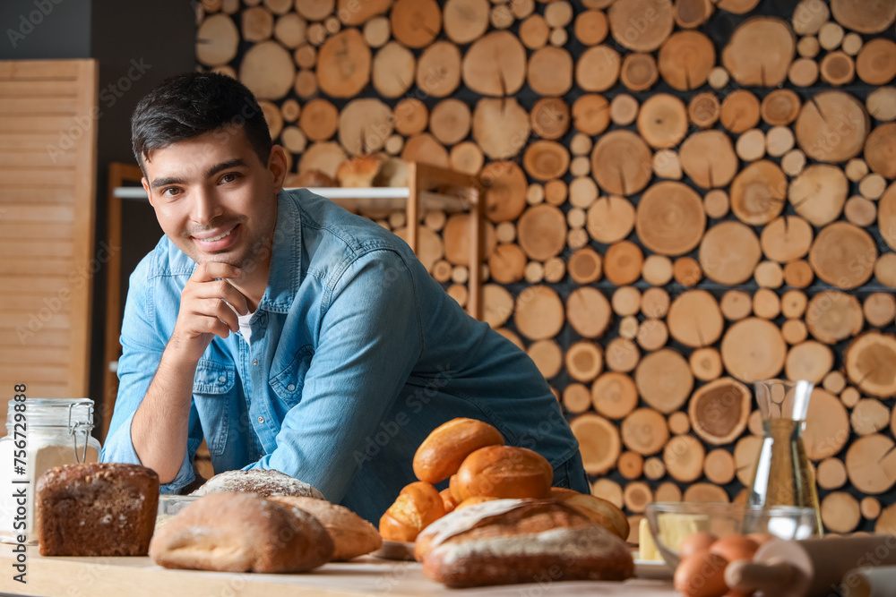 Young man with loaves of fresh bread at table in bakery