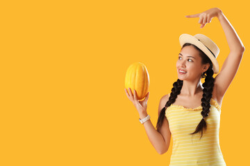 Poster - Beautiful young Asian woman with whole fresh melon pointing at something on yellow background