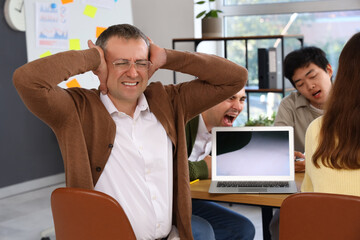 Canvas Print - Mature businessman suffering from noisy colleagues in office