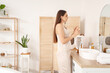 © Pixel-Shot - Beautiful young woman with jar of cream and small refrigerator for cosmetic products in bathroom